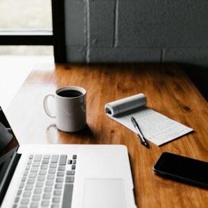 Laptop, notebook, and coffee on a wooden desk — IT Guy Reno